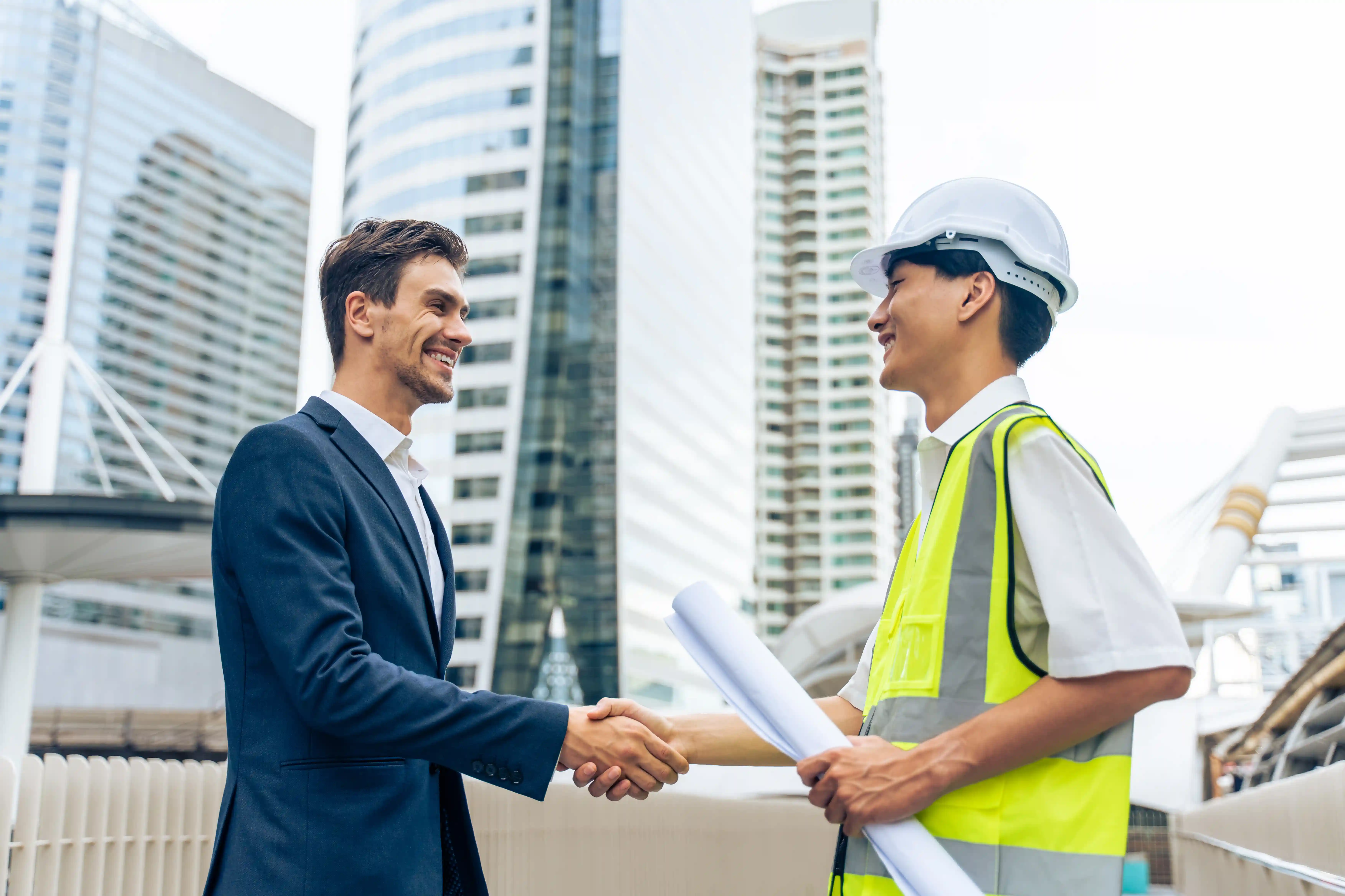 man in business suit shaking hands with man in construction vest and hat